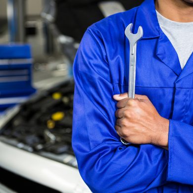 Mid section of mechanic with arms crossed holding spanner at repair garage